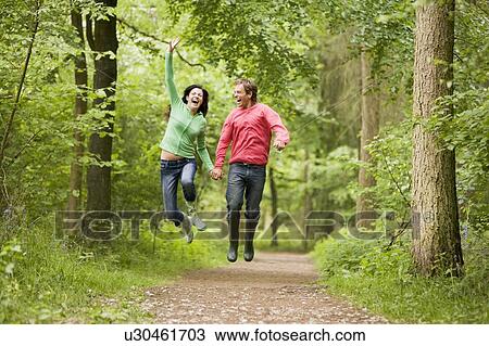 Stock Image - Couple jumping on path holding hands and smiling. Fotosearch