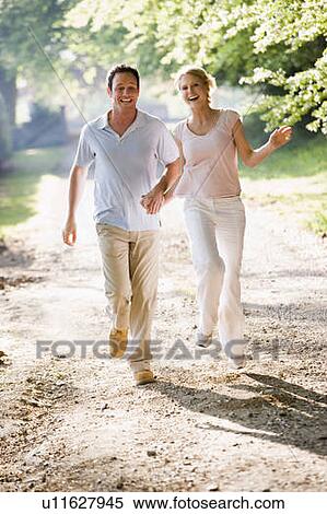 Couple running outdoors holding hands and smiling View Large Photo Image Stock Photography - Couple running outdoors holding hands and smiling. Fotosearch