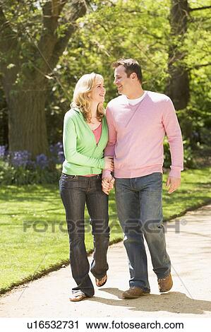 Stock Image - Couple walking on path holding hands smiling. Fotosearch