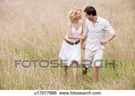Stock Photograph - Couple walking outdoors holding hands smiling. Fotosearch