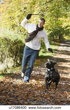 Man outdoors with dog on path in park holding branch smiling (selective focus) View Large Photo Image Stock Image - Man outdoors with dog on path in park holding branch smiling (selective focus). Fotosearch