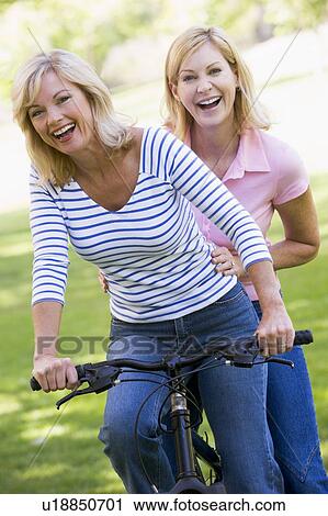 Stock Image - Two friends on one bike outdoors smiling. Fotosearch