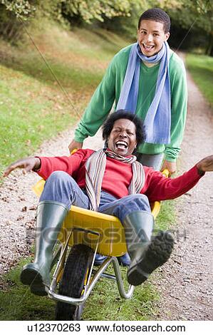 Young boy outdoors pushing mother in wheelbarrow and smiling (selective focus) View Large Photo Image Stock Image - Young boy outdoors pushing mother in wheelbarrow and smiling (selective focus). Fotosearch