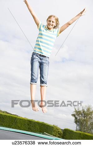 Stock Photo - Young girl jumping on trampoline smiling. Fotosearch