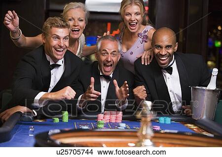 Picture - Five people in casino playing roulette smiling (selective focus). Fotosearch