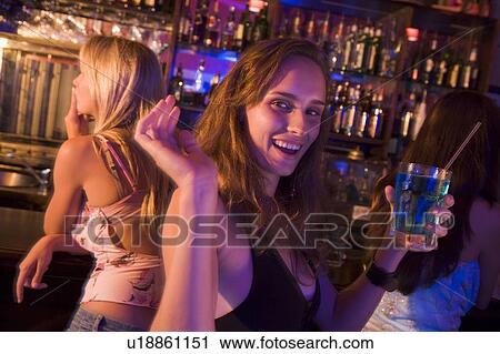 Stock Image - Young woman in a bar with friends. Fotosearch