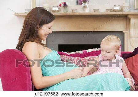 Pregnant mother with daughter in living room touching belly and smiling View Large Photo Image Stock Image - Pregnant mother with daughter in living room touching belly and smiling. Fotosearch