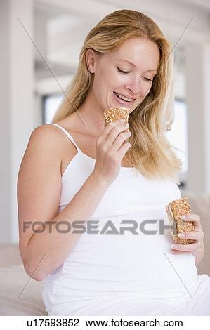 Stock Image - Pregnant woman eating bread and smiling. Fotosearch
