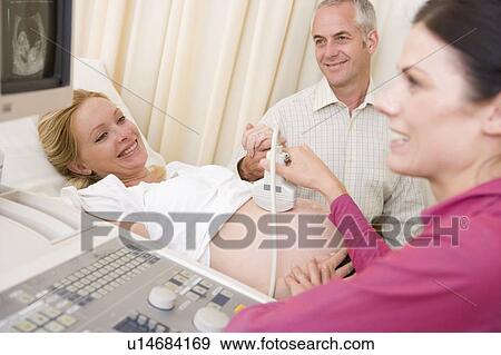 Stock Photo - Pregnant woman getting ultrasound from doctor with husband watching. Fotosearch