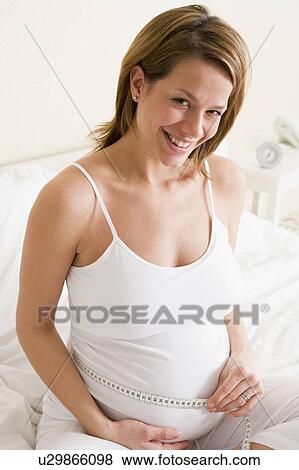 Pregnant woman in bedroom measuring belly smiling View Large Photo Image Stock Photo - Pregnant woman in bedroom measuring belly smiling. Fotosearch