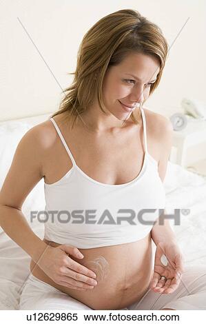 Pregnant woman in bedroom rubbing cream on belly smiling View Large Photo Image Stock Photography - Pregnant woman in bedroom rubbing cream on belly smiling. Fotosearch