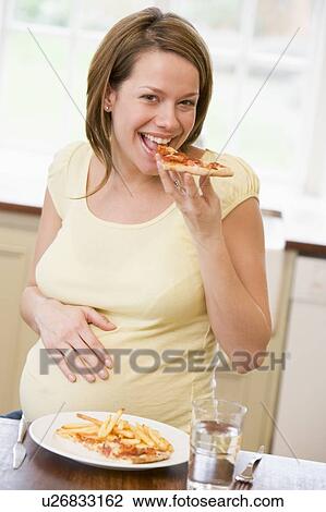 Pregnant woman in kitchen eating French fries and pizza smiling View Large Photo Image Stock Image - Pregnant woman in kitchen eating French fries and pizza smiling. Fotosearch