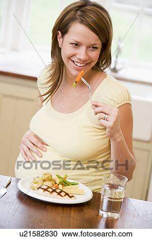 Pregnant woman in kitchen eating chicken and vegetables smiling View Large Photo Image Stock Image - Pregnant woman in kitchen eating chicken and vegetables smiling. Fotosearch