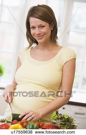 Stock Photo - Pregnant woman in kitchen making a salad smiling. Fotosearch