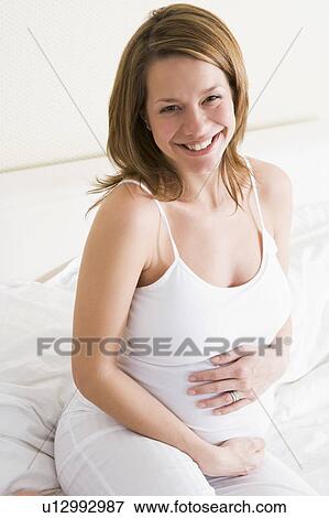 Stock Photo - Pregnant woman sitting in bed smiling. Fotosearch