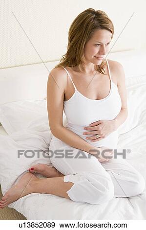 Stock Photo - Pregnant woman sitting in bed smiling. Fotosearch