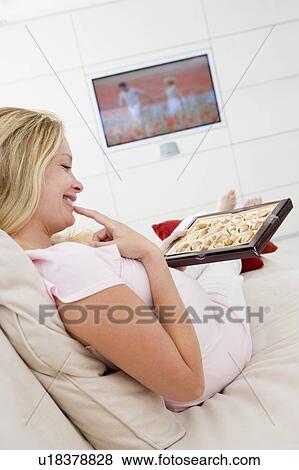 Pregnant woman watching television and eating chocolates smiling View Large Photo Image Stock Photo - Pregnant woman watching television and eating chocolates smiling. Fotosearch