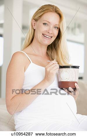 Stock Photo - Pregnant woman with bucket of ice cream smiling. Fotosearch