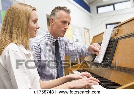 Stock Image - Female student learning piano with teacher in classroom. Fotosearch