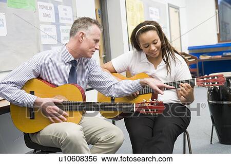 Female student receiving guitar lesson from teacher in classroom View Large Photo Image Stock Photograph - Female student receiving guitar lesson from teacher in classroom. Fotosearch