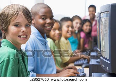 Stock Image - Six children at computer terminals with teacher in background (depth of field/high key). Fotosearch