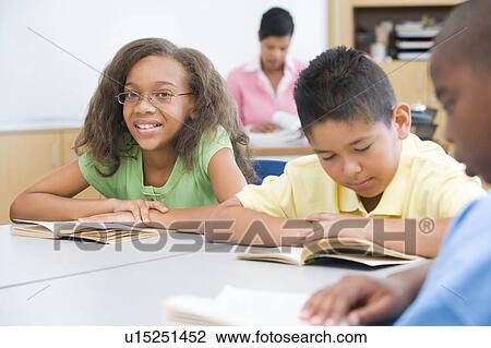 Stock Image - Students in class reading with teacher in background (selective focus). Fotosearch