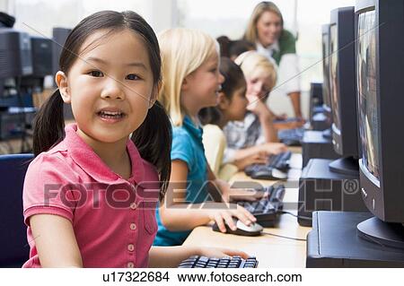 Picture - Children at computer terminals with teacher in background (depth of field/high key). Fotosearch