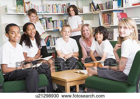 Stock Image - Seven students in library reading books with teacher. Fotosearch