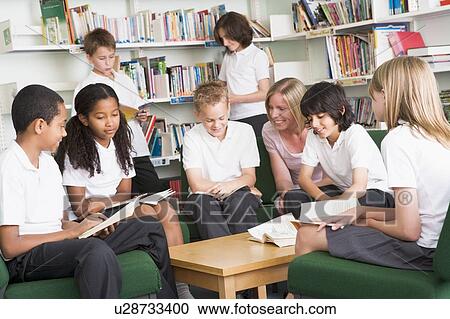 Stock Image - Seven students in library reading books with teacher. Fotosearch