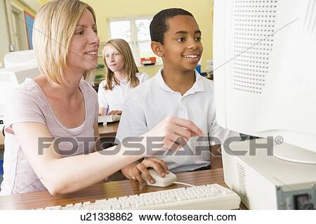 Stock Image - Student and teacher at computer terminal with student in background. Fotosearch