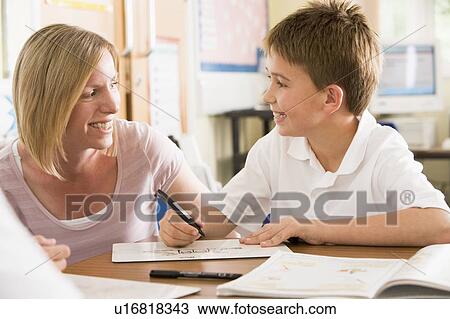 Stock Image - Student in class taking notes with teacher helping. Fotosearch