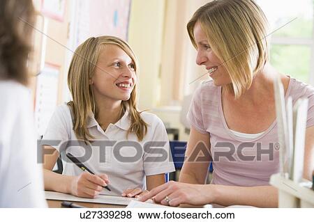 Stock Photo - Student in class taking notes with teacher helping. Fotosearch