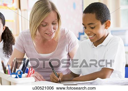 Stock Photograph - Student in class taking notes with teacher helping. Fotosearch