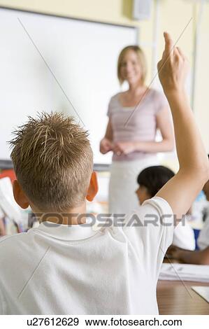 Stock Photo - Student volunteering in class with teacher at board (selective focus). Fotosearch