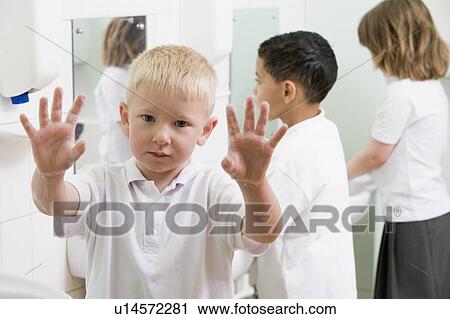 Stock Image - Students in bathroom at sinks washing hands with one holding up soapy hands (selective focus). Fotosearch
