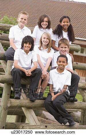 Stock Image - Seven students sitting on wooden structure outdoors. Fotosearch
