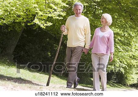 Stock Image - Couple walking on path in park holding hands and smiling. Fotosearch