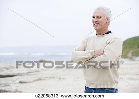 Stock Image - Man at the beach with arms crossed smiling. Fotosearch