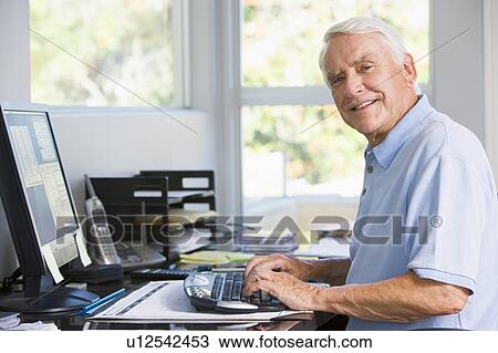 Stock Image - Man in home office using computer smiling. Fotosearch