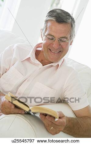 Man in living room reading book smiling View Large Photo Image Stock Photo - Man in living room reading book smiling. Fotosearch