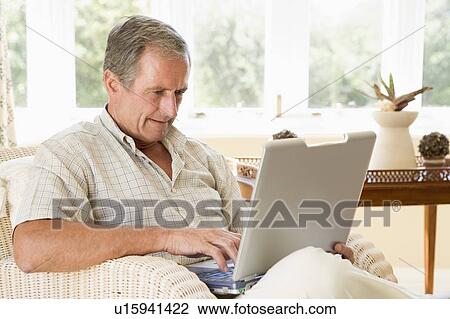 Stock Image - Man in living room with laptop. Fotosearch