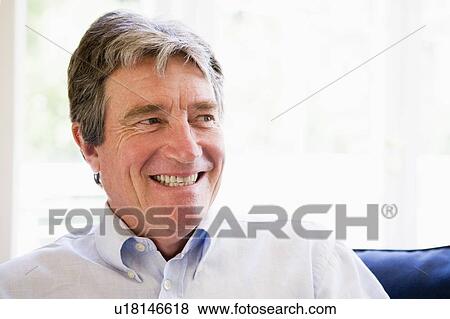 Stock Photo - Man sitting in living room smiling. Fotosearch