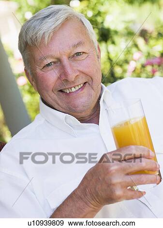 Stock Photo - Senior man sitting outdoors with a glass of orange juice. Fotosearch