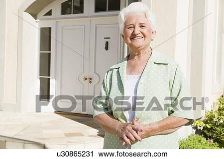 Stock Image - Senior woman standing outside her home. Fotosearch