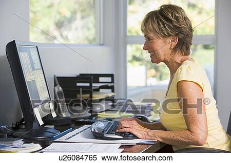 Stock Photography - Woman in home office using computer smiling. Fotosearch