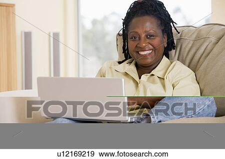 Stock Photo - Woman in living room using laptop and smiling. Fotosearch