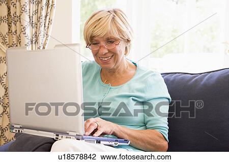 Stock Image - Woman in living room with laptop smiling. Fotosearch