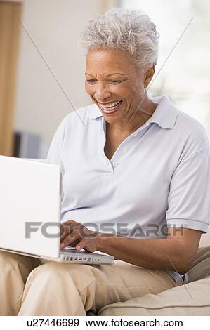 Stock Photo - Woman in living room with laptop smiling. Fotosearch