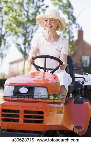 Stock Photo - Woman outdoors driving lawnmower smiling. Fotosearch
