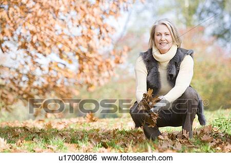 Stock Photograph - Woman outdoors holding leaves and smiling (selective focus). Fotosearch